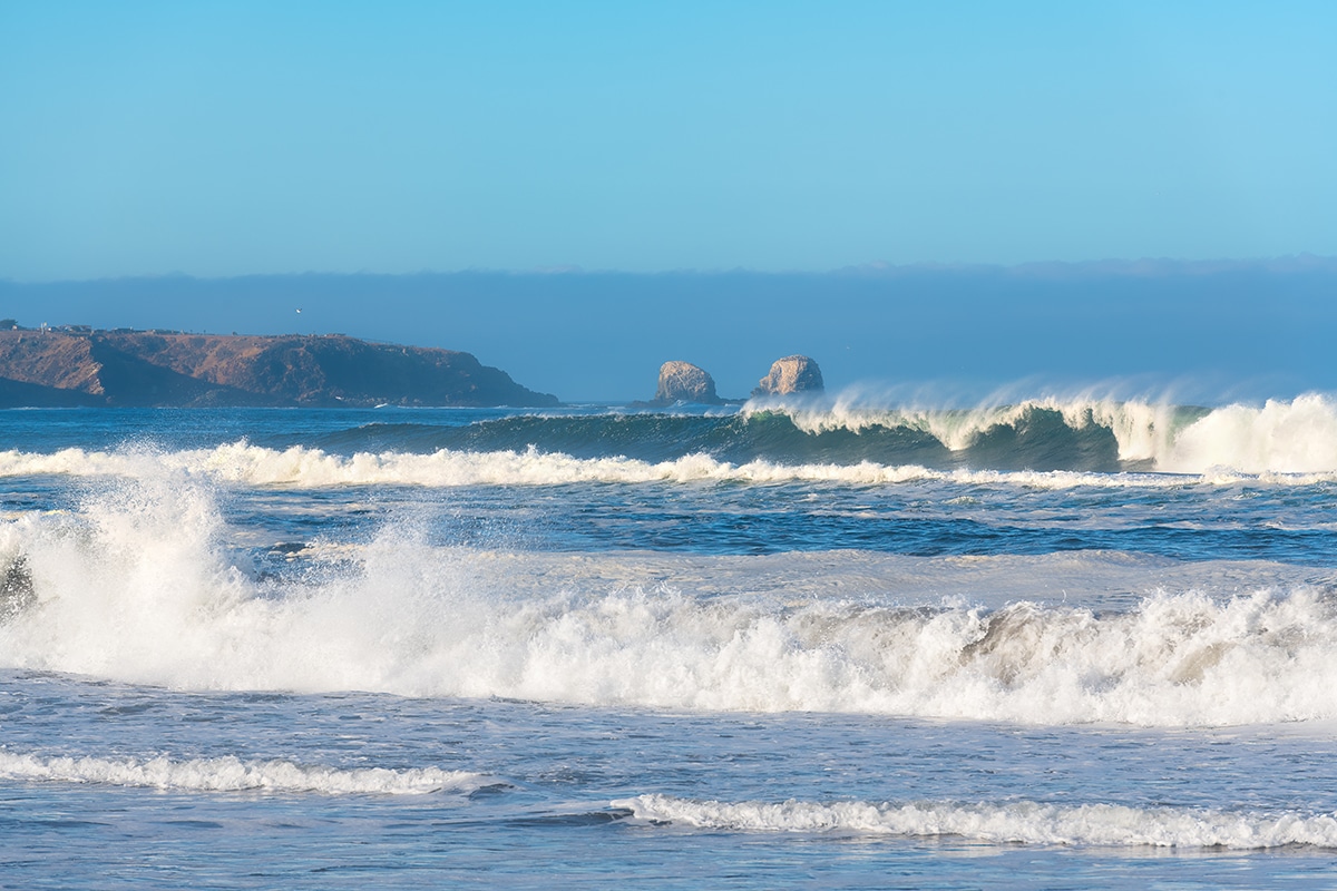 Waves braking in the beach of Pichilemu with the cliffs of Punta de Lobos in the back